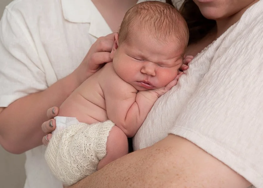 Newborn photographer Melbourne image of sleeping newborn baby sleeping on her mother's chest with her father cuddling her