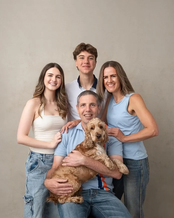 Studio image of a family of four smiling looking at the camera with their golden cocker spaniel dog