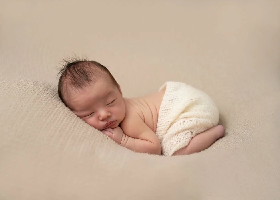 Susan Bradfield Photography of a newborn baby sleeping on his tummy wearing cream bloomers on a taupe background.