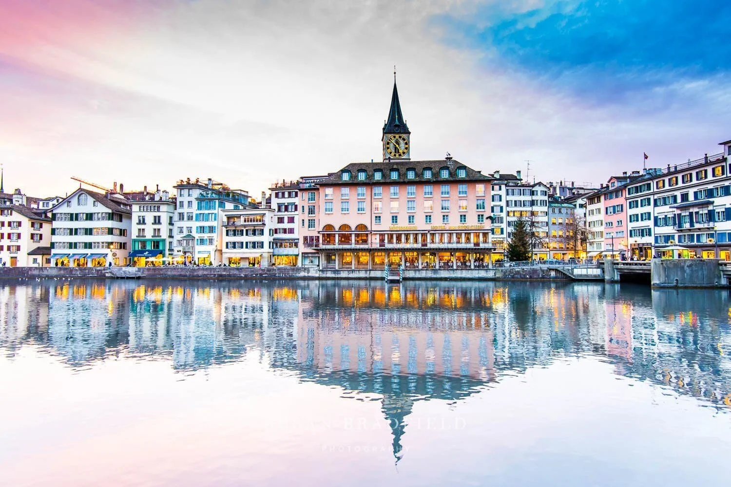 Susan Bradfield Photography image of the Storchen Hotel in Zurich, Switzerland and sunset. The sky is pink, blue and white with a reflection on the Limmat