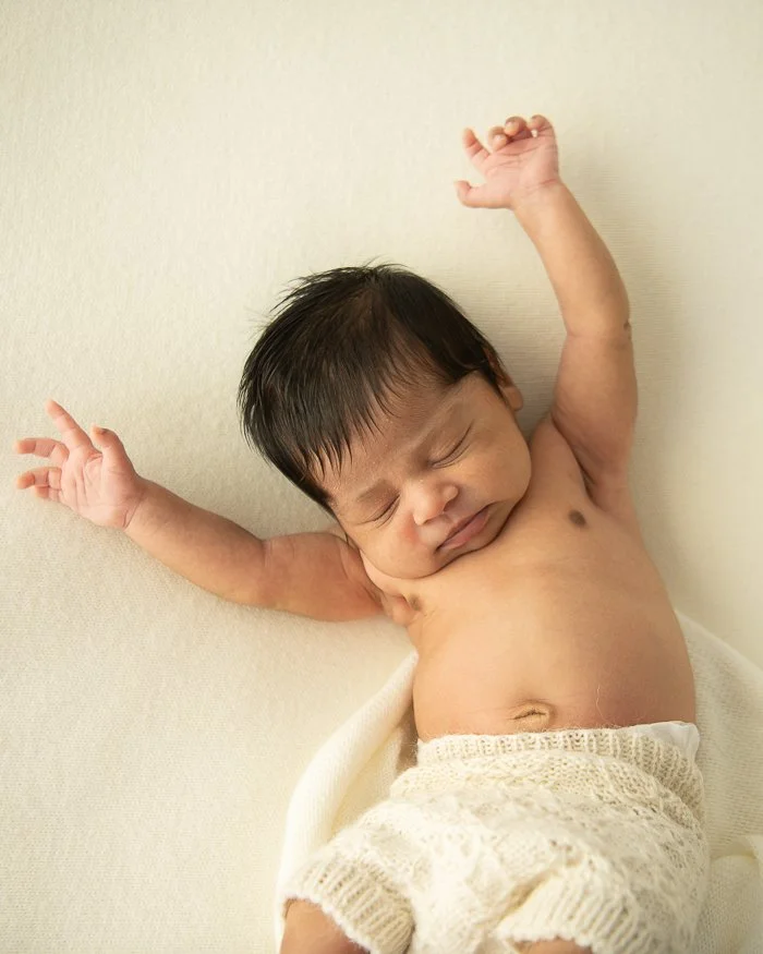 Image of a newborn baby wearing bloomers having a big stretch with both arms reaching out