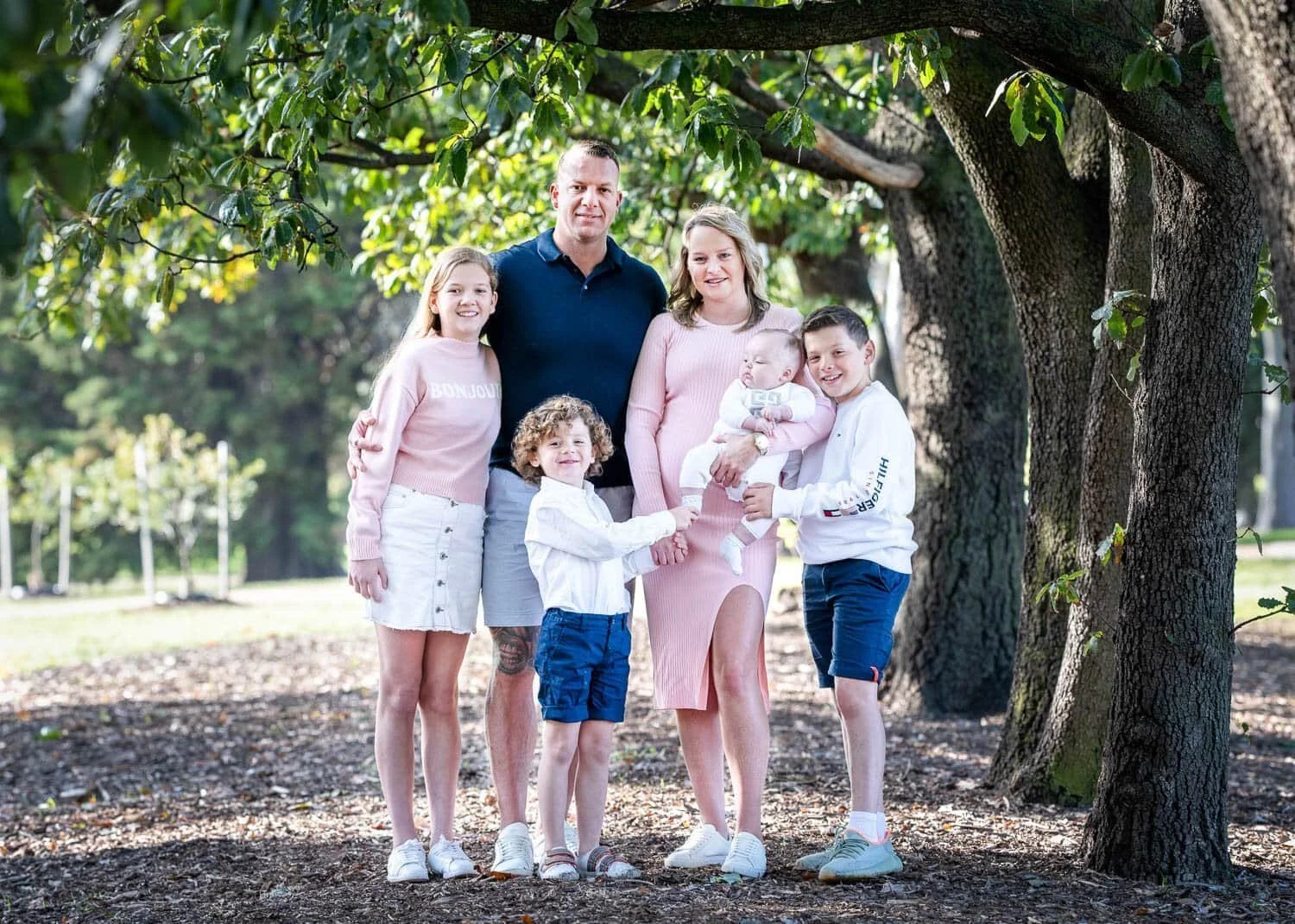 Susan Bradfield Photography family photo of a group of six dressed in pink, white and blue sitting happily at the park