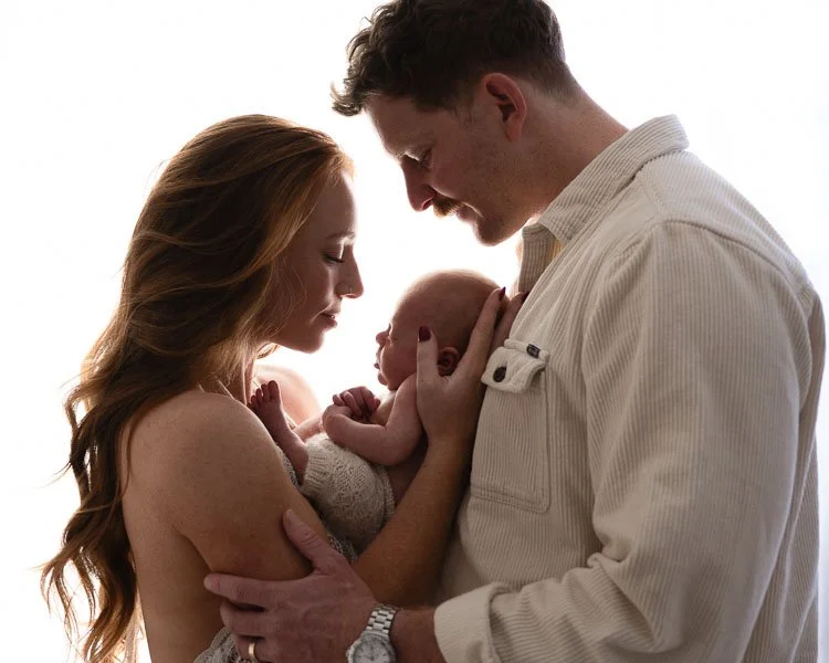 Susan Bradfield Photography backlit image of two parents side on looking at newborn baby