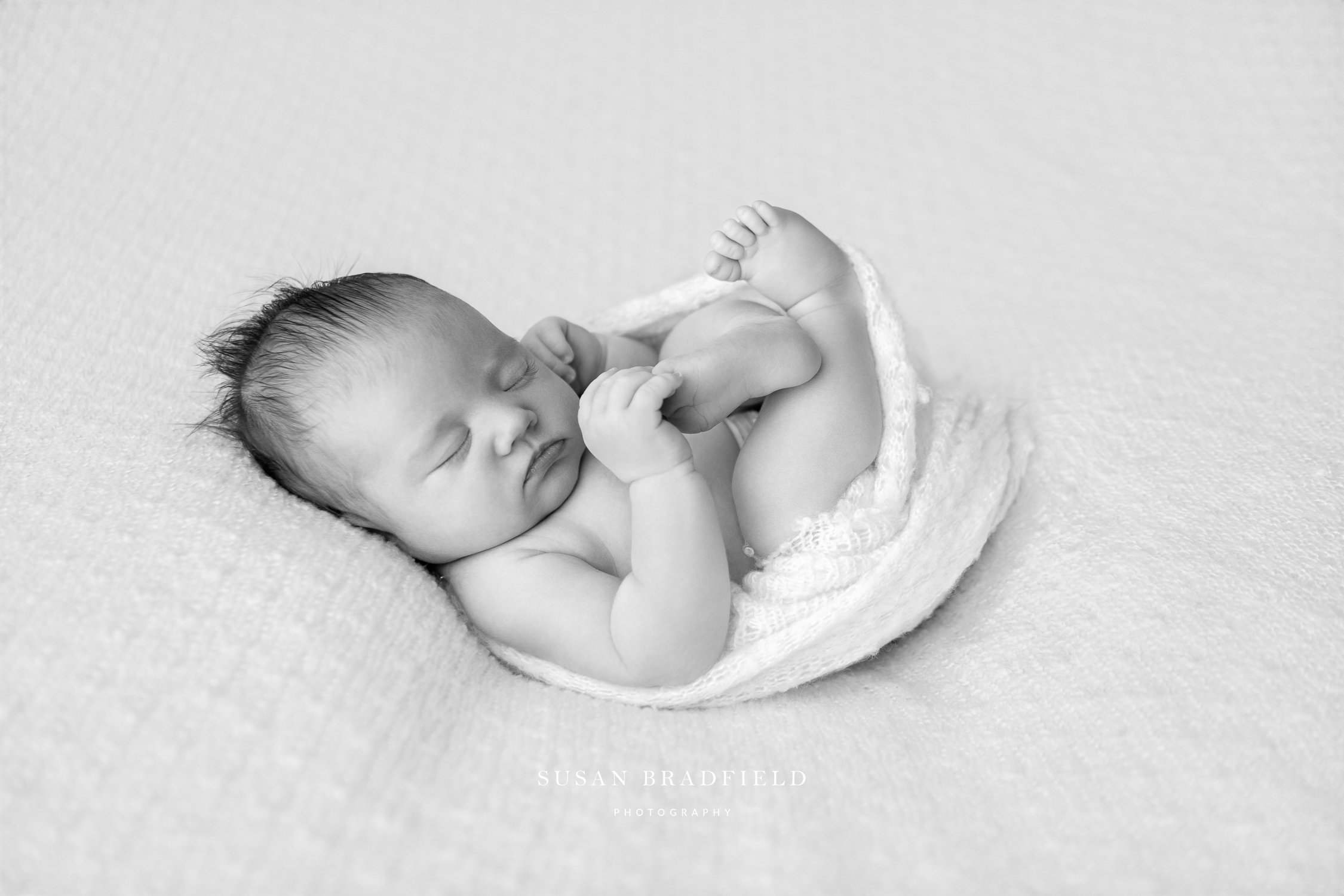 Monochrome image of a sleeping baby curled up holding his foot