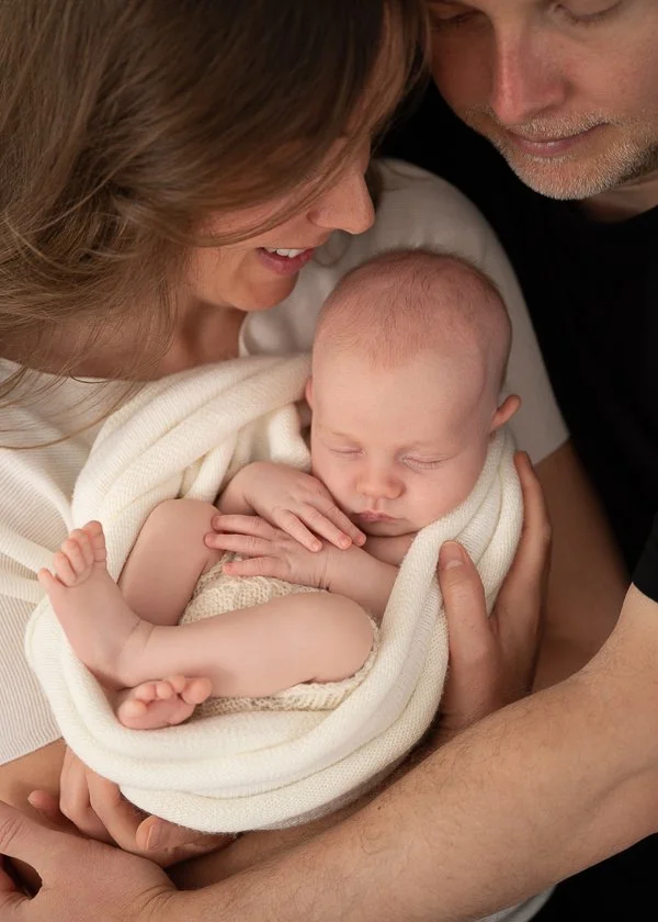 Nebworn photographer photo of curled up sleeping baby held by mother and watched by father