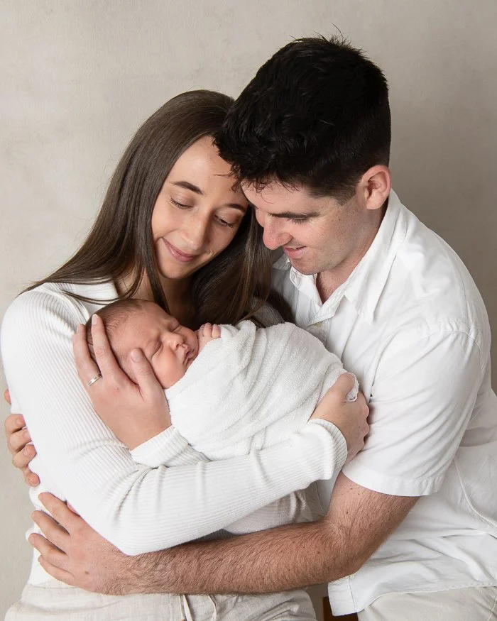 Newborn photography Image of a loving mother and father holding their newborn baby in their arms and smiling looking at her