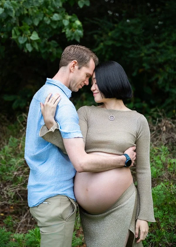 Maternity photography Melbourne photo of a pregnant woman wearing a gold skirt and top showing her pregnant belly holding her male partner in a garden setting