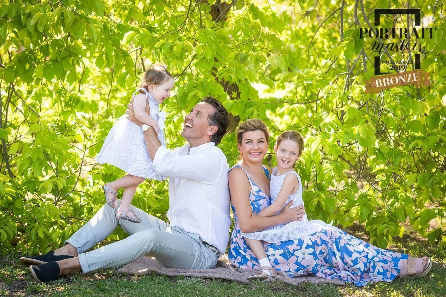 Happy faily of parents with their two girls sitting in a park very joyful