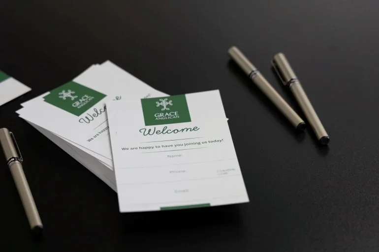 Welcome cards from Grace Anglican Church with pens on a black table