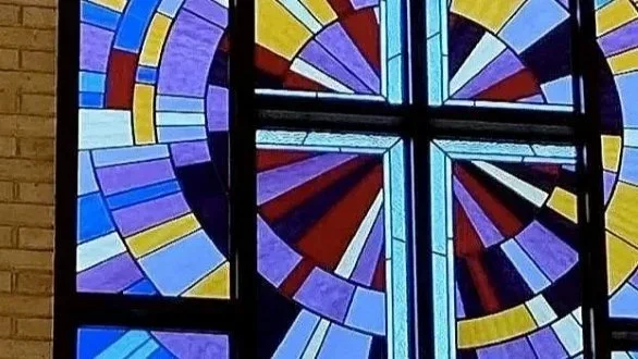 Colorful geometric stained-glass window with blue, purple, red, yellow, and white segments in a cross-shaped design