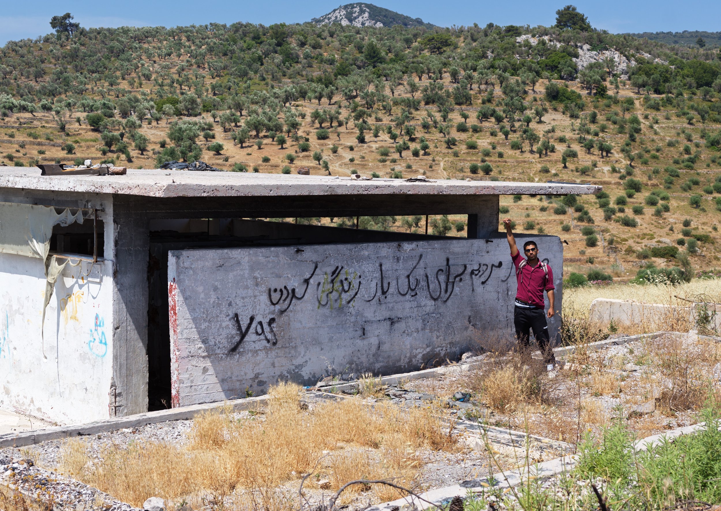 Mohammed bij de muur met zijn eigen graffiti op het terrein van het voormalige vluchtelingenkamp Moria op Lesbos