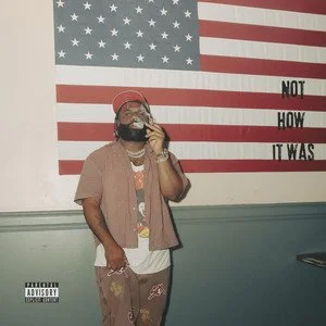 Person taking a mirror selfie in front of a large American flag mural with the words 'NOT HOW IT WAS' written on it.