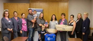 Representatives of Connected Forever and Dugan-Kramer Funeral Chapel present a CuddleCot™ to staff of the Regional West Birth and Infant Care Center. From left: Julie Meier, RN; Catharine Houstoun, RN; Sara Kraft-Leavitt, RN; Jesse Pella holding Frannie Pella; Tracy Pella holding Maybry Pella; Cooper Pella; Erika Carmody, MSN, RN; Melissa Schaub, MSN, RN; Kayla Sorell, BSW; Tammy Lutz, Mary Beth Mau.