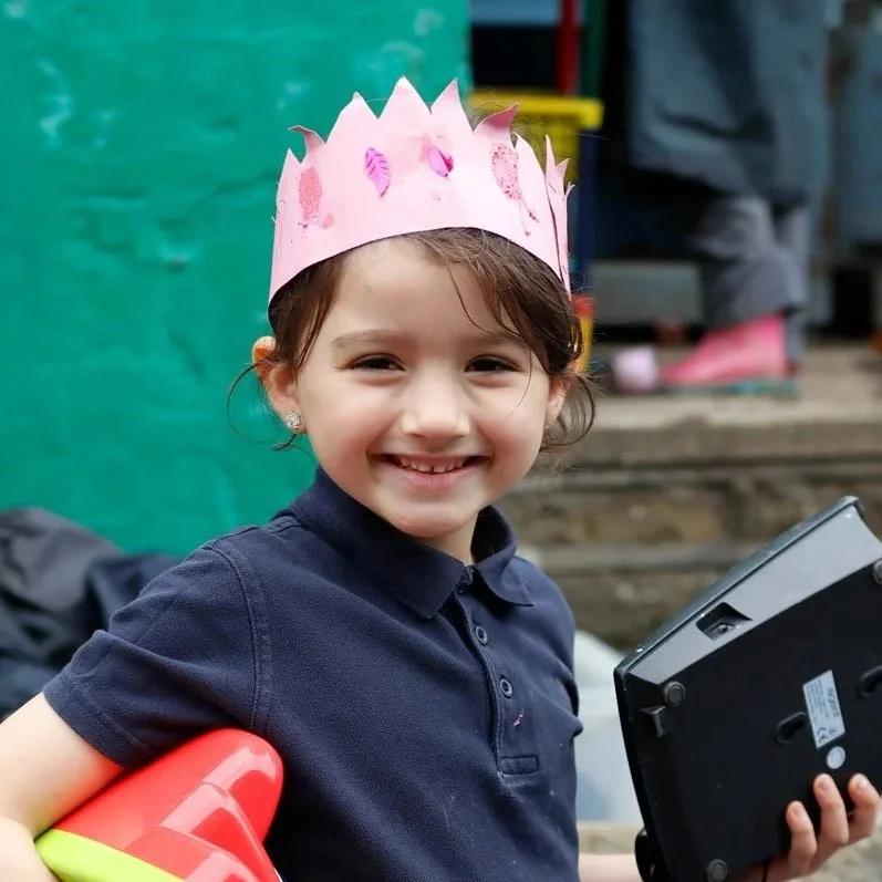 A girl smiles, whilst wearing a hand made paper crown