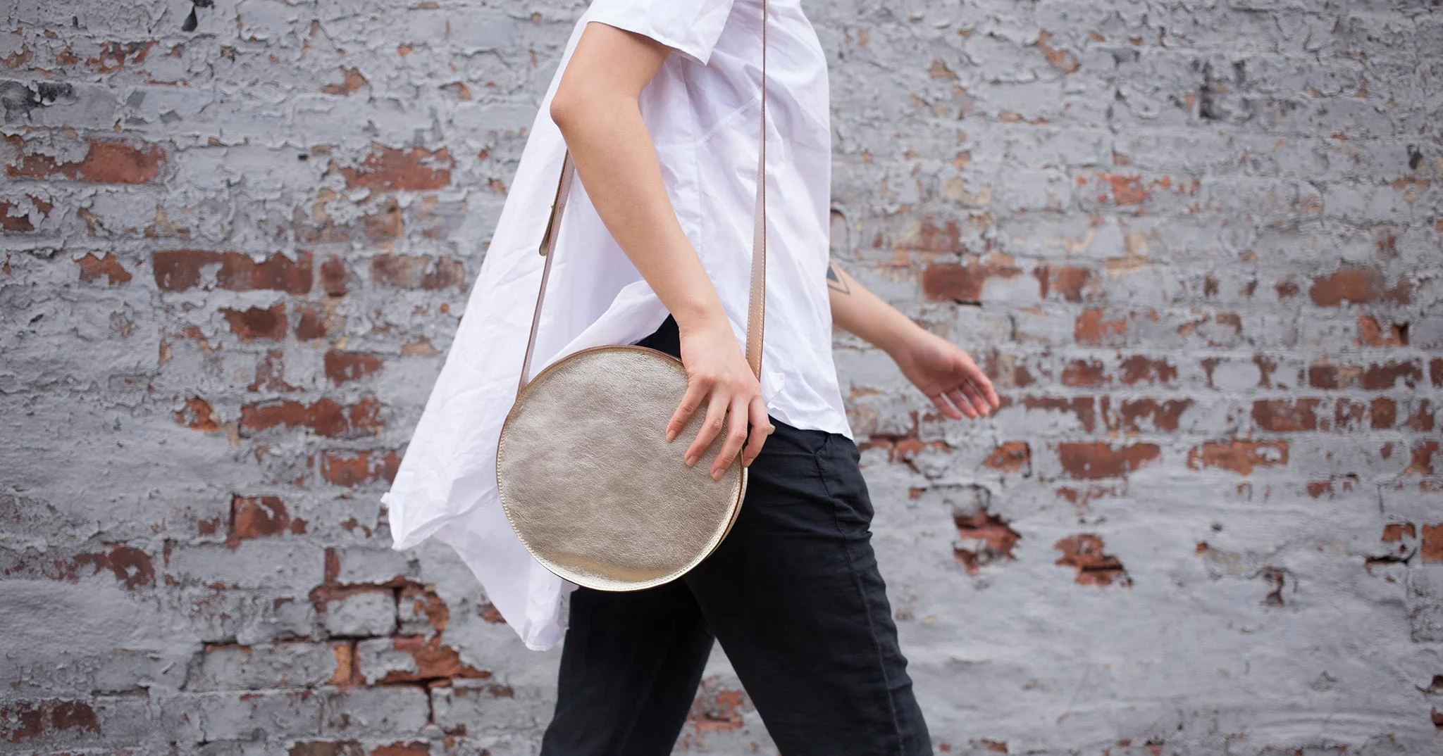 nyc graphic designer art director MH minor history leather goods product accessories design art direction moon crossbody bag white gold shirt brick wall walking black pants working girl