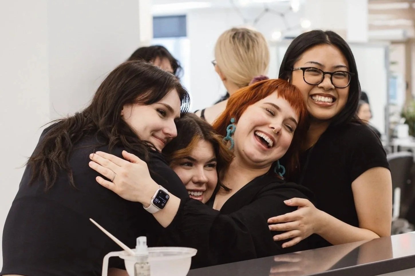Four students hugging each other in front of the colour bar, celebrating and sharing a moment of connection during student life at AIW