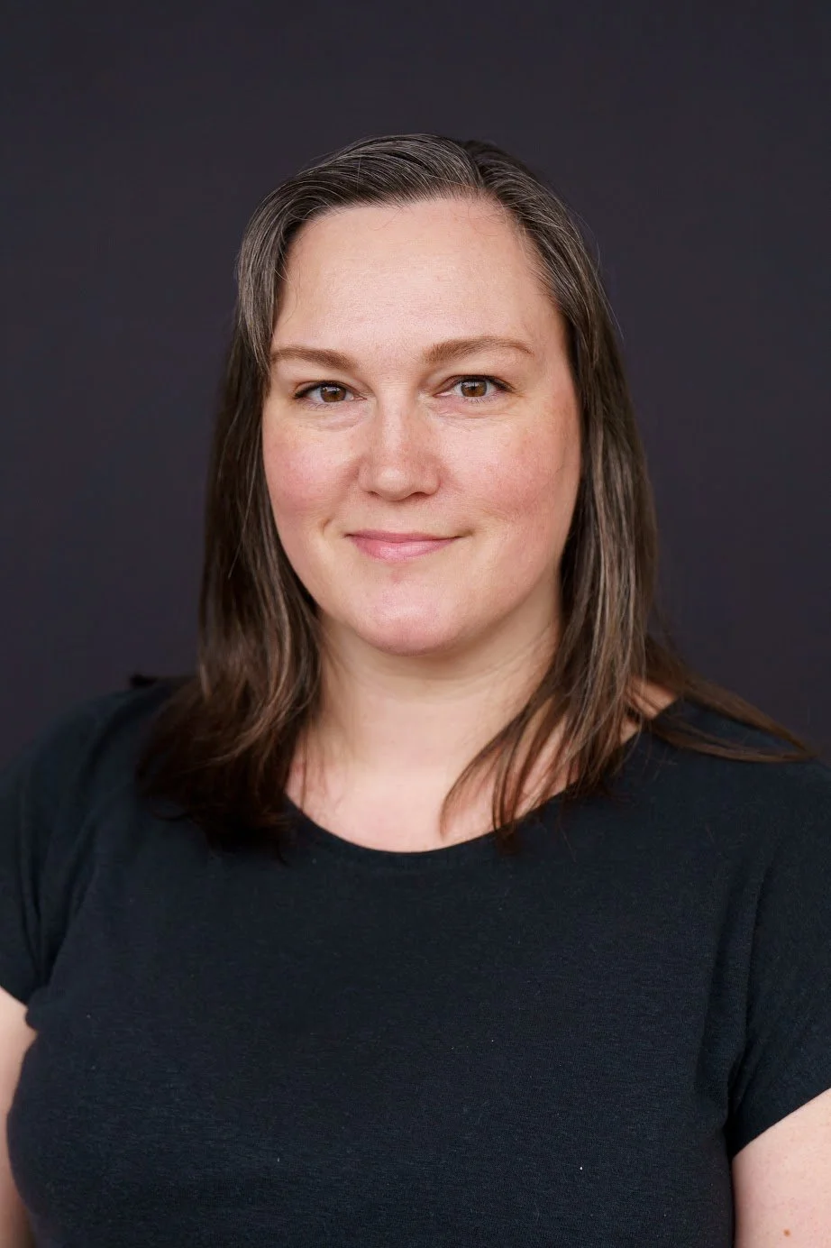 Image of Registrar, Christine, who has brown hair and is wearing a black t-shirt against a black background