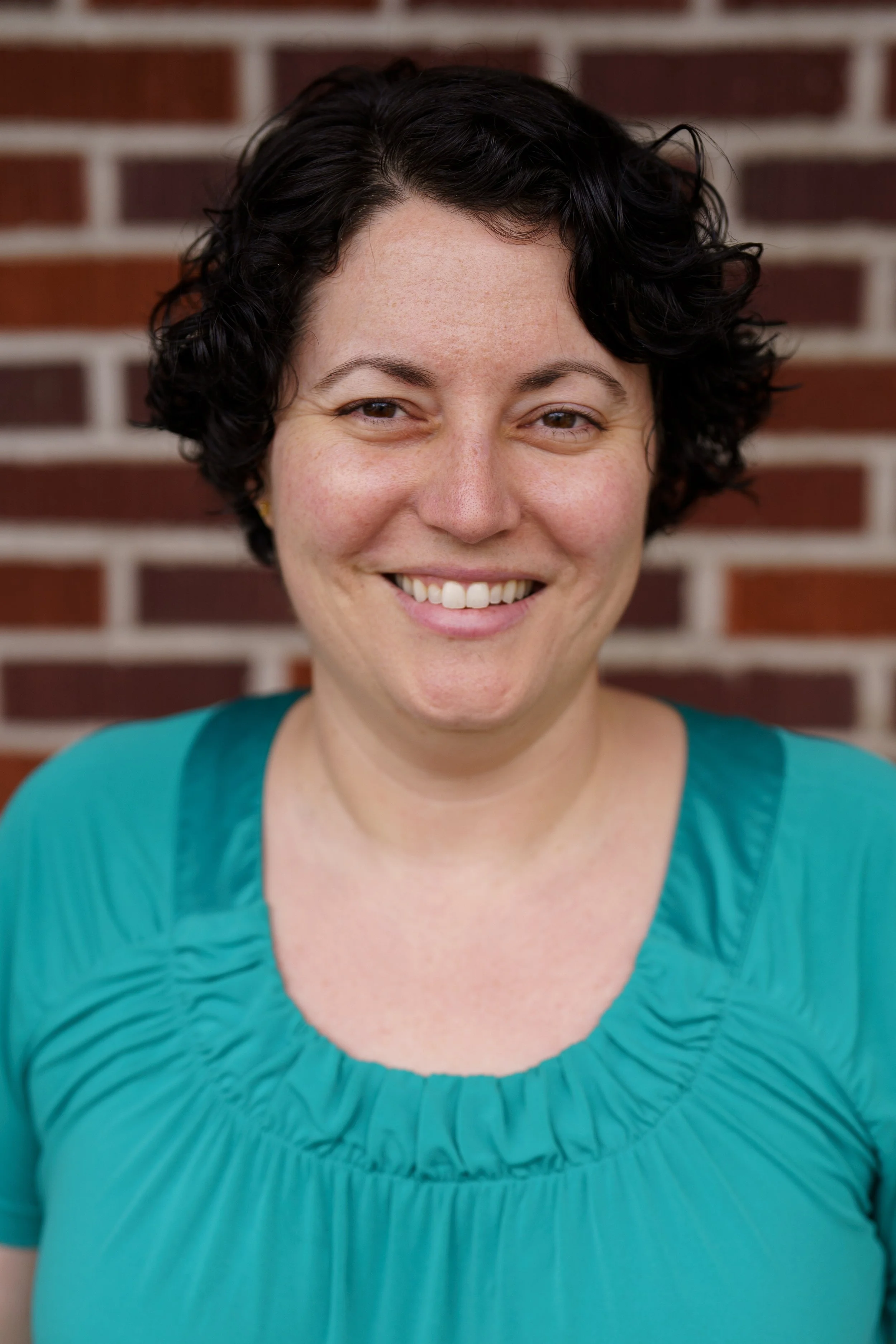 Picture of Coop President Katie Donovan who has short dark curly hair, ad big smile, and is wearing a teal shirt.