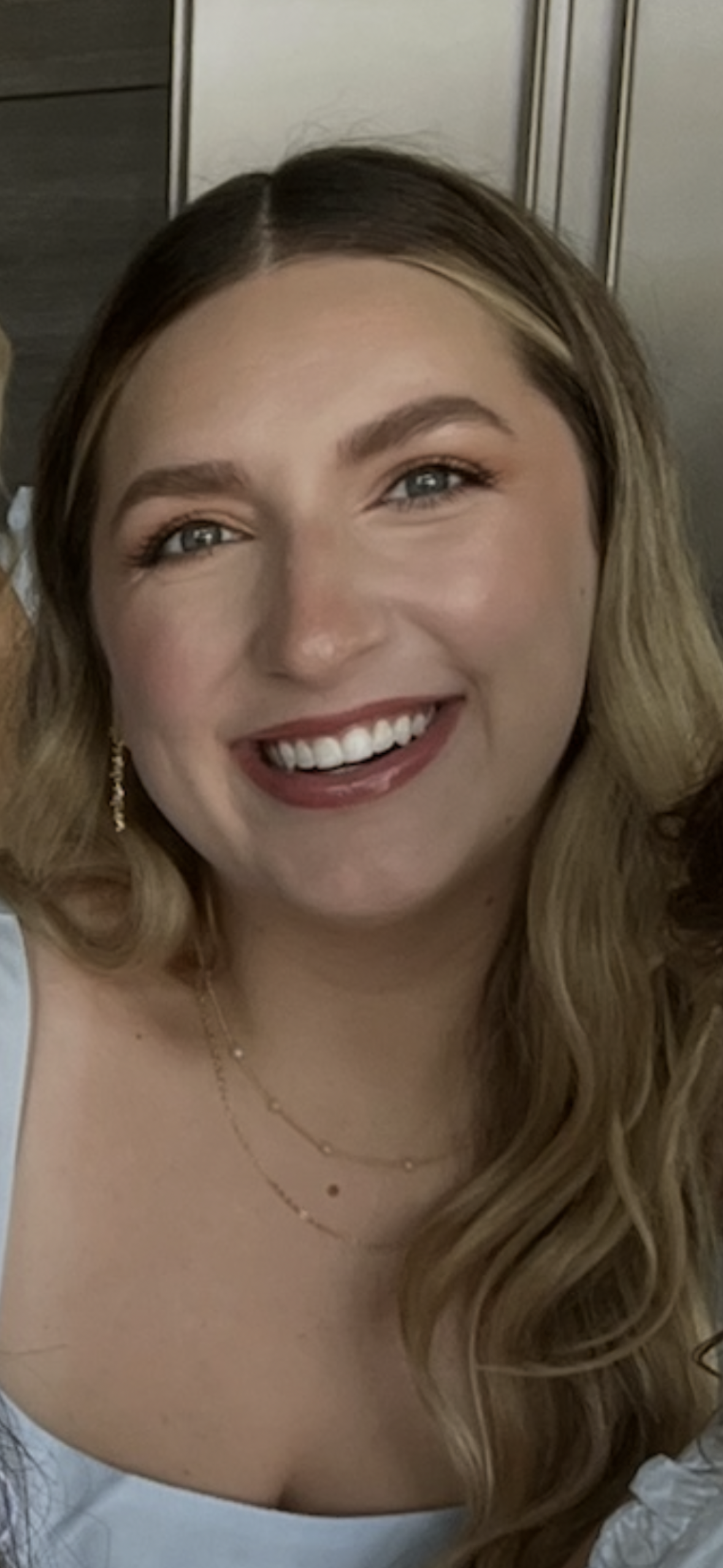 Photo of Mrs. Burns who has long medium blonde hair, a big smile, and is wearing a light blue top with gold necklaces.