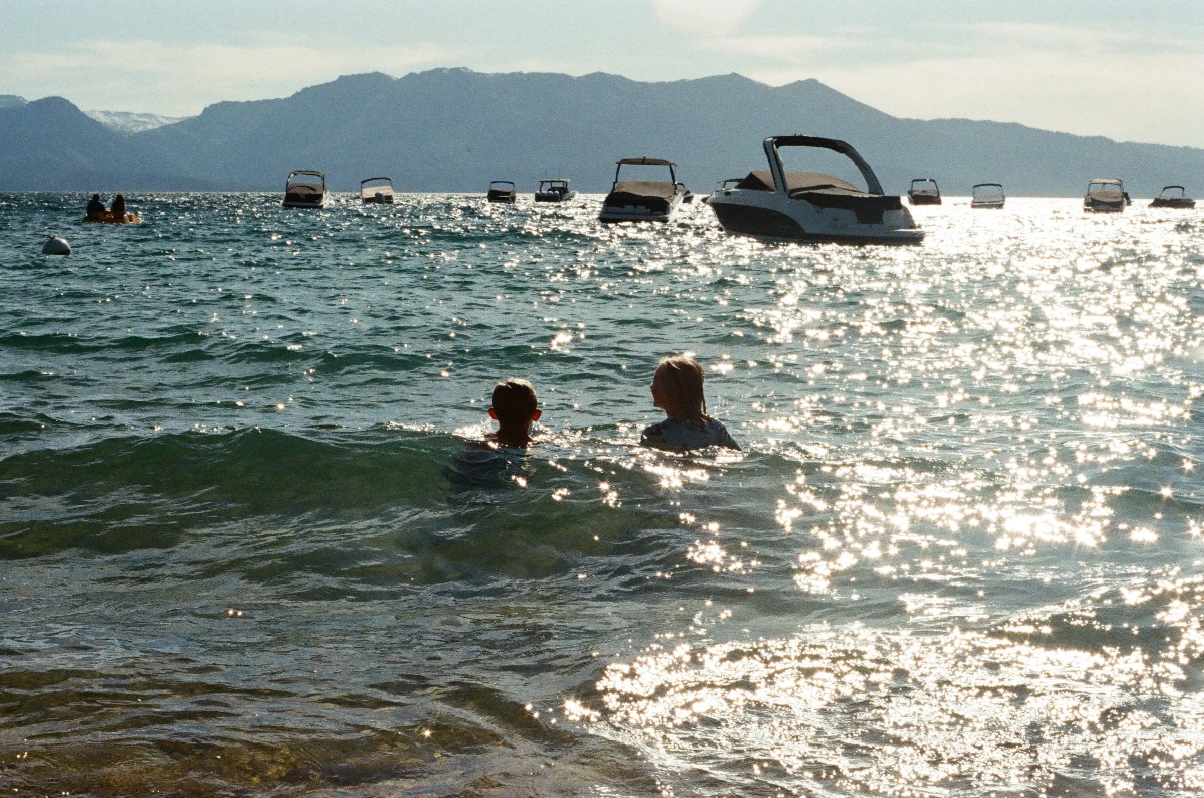 swimming in the lake with boats floating on the water and mountains in the background.