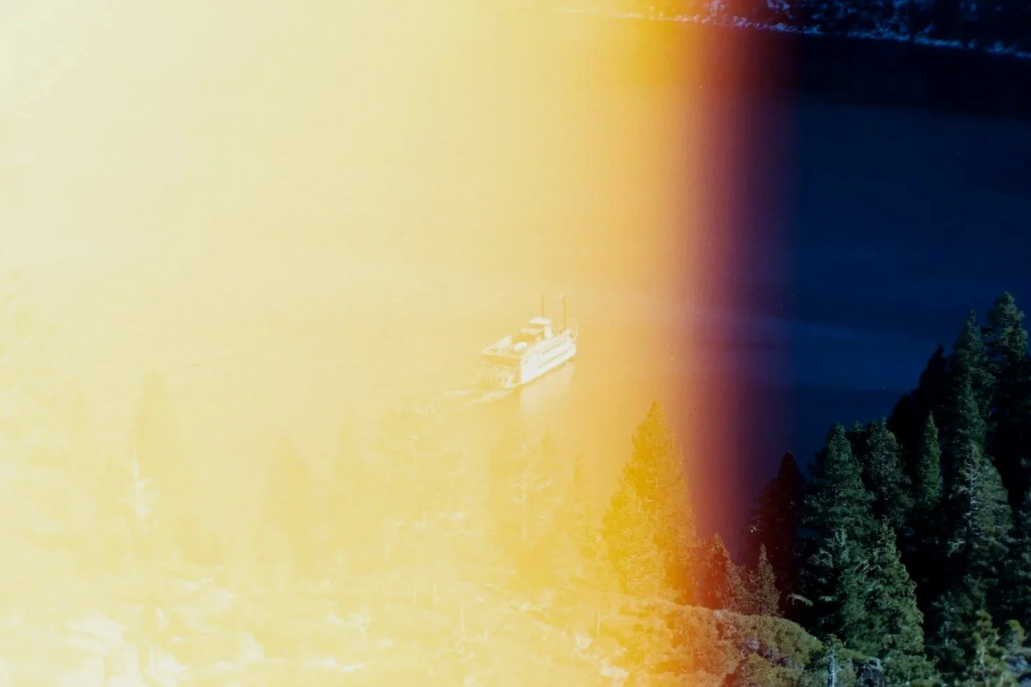 Mid 35mm film exposure photo of a ferry boat on a body of water, with trees on the right side and a light leak effect creating a yellow and purple gradient across the image.