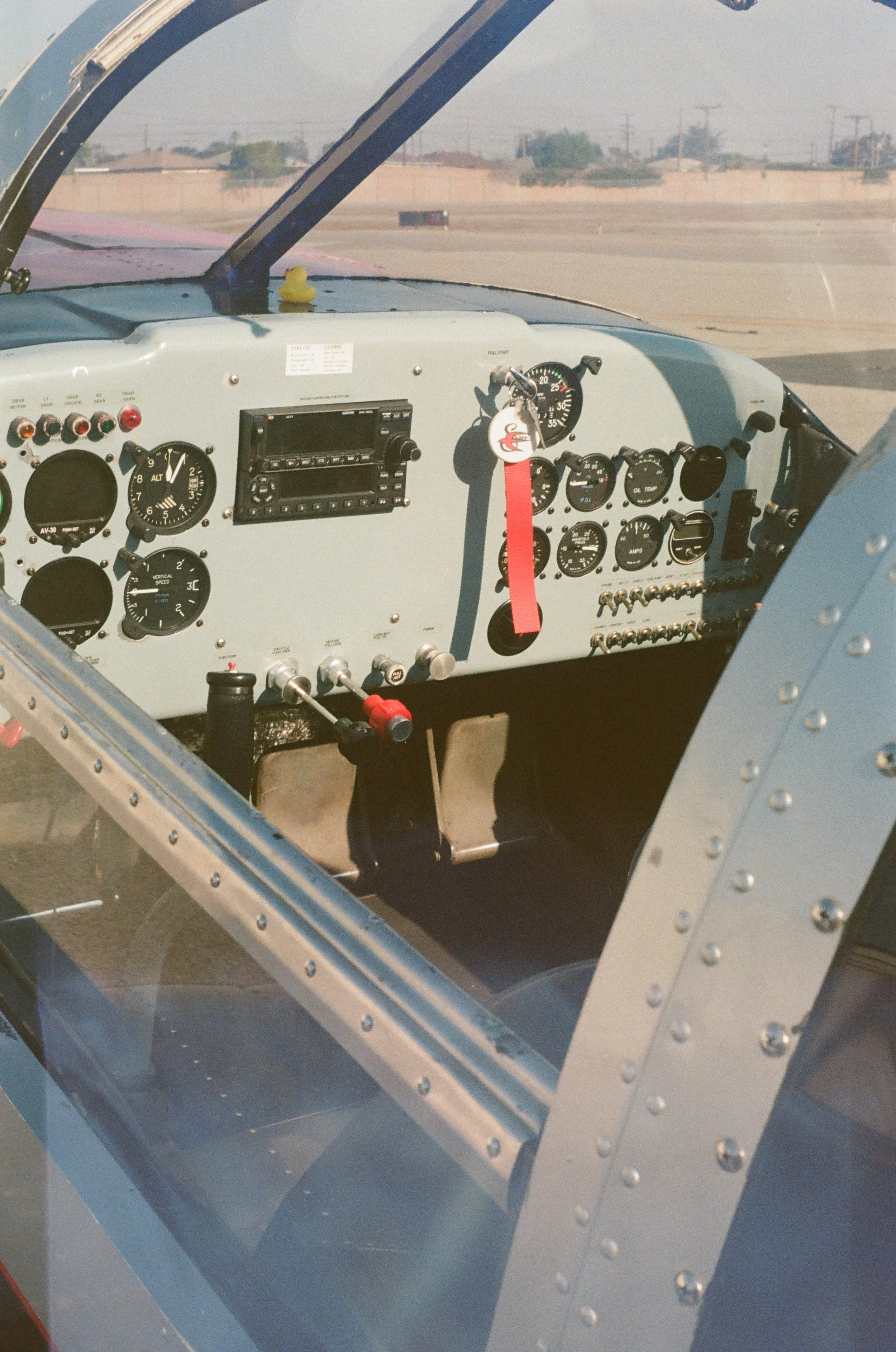 Interior of an airplane cockpit with various gauges, switches, and controls, viewed from outside through the windshield.