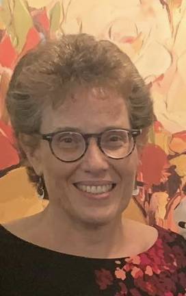 A woman with short, curly hair and glasses, smiling in front of a vibrant, floral background.