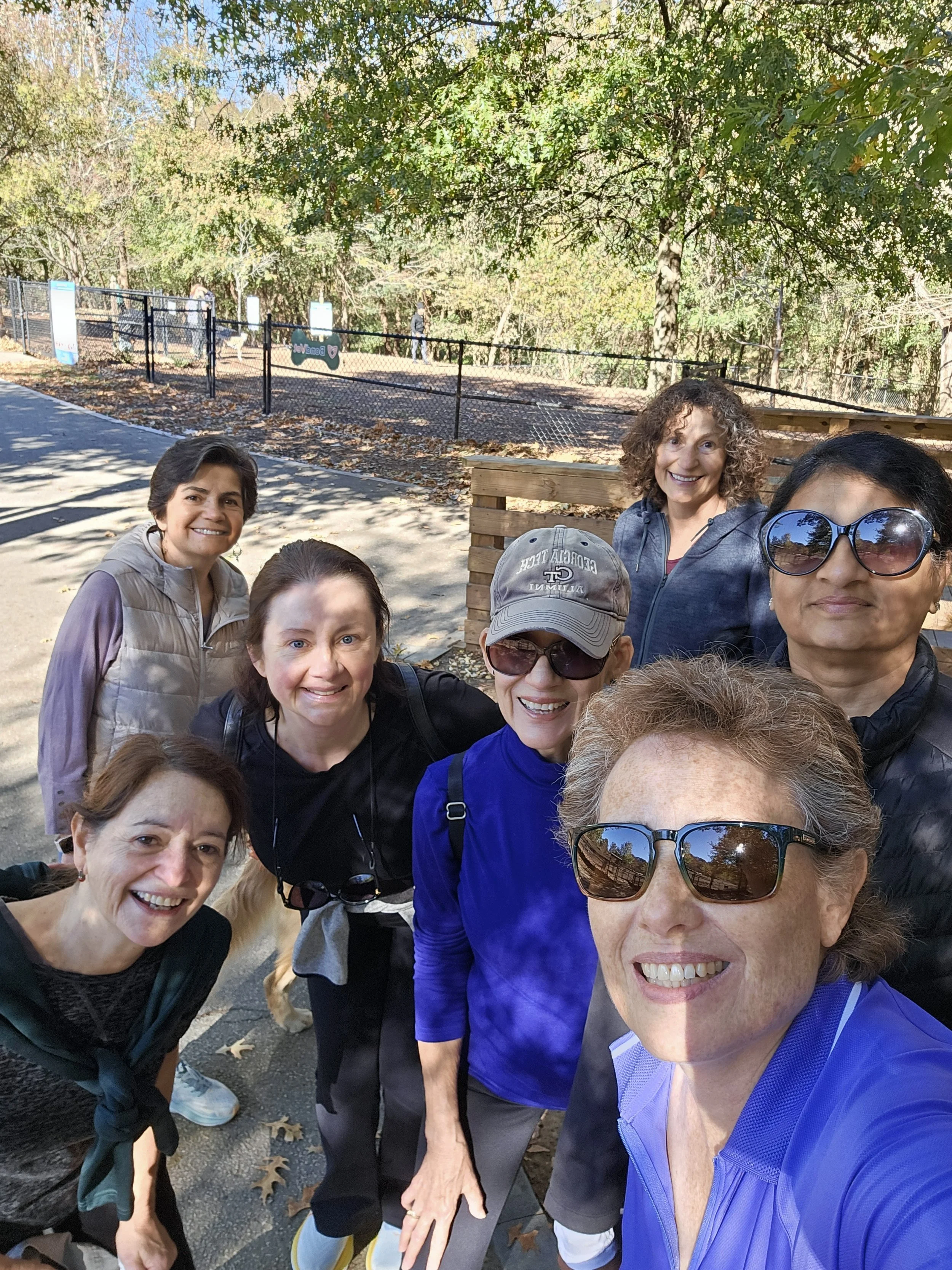 Group of smiling women taking a selfie outdoors on a sunny day with trees in the background. This is for a walking group in the Atlanta area.