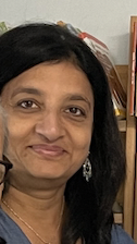 Close-up of a woman with black hair and earrings in an indoor setting.