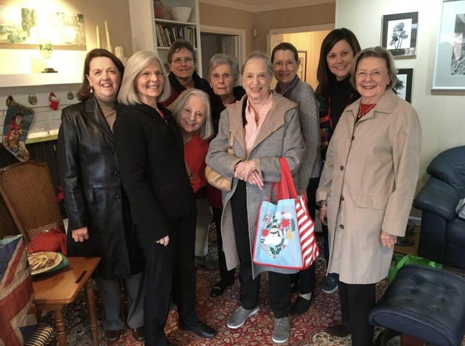Group of nine women gathered in a living room, smiling during during daytime book group meeting