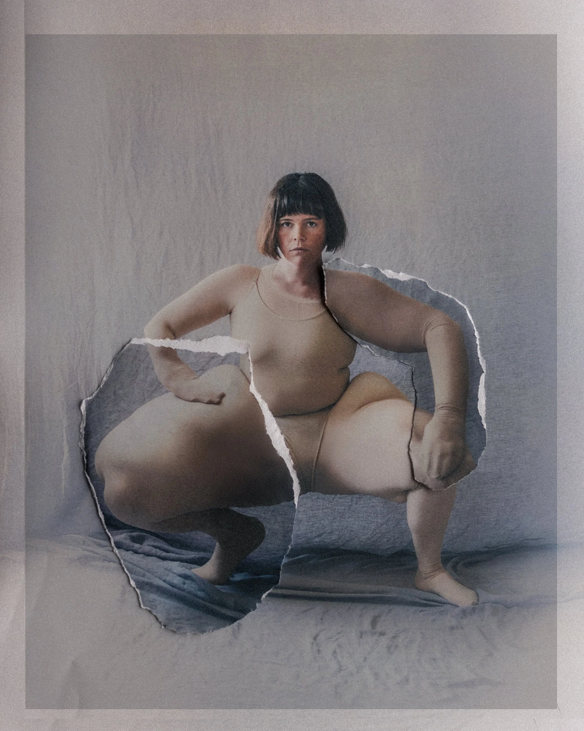 A woman with short dark hair squats on the floor with a neutral expression, looking directly at the camera. She is wearing nude-colored clothing. The photo includes a torn paper effect, creating a layered, surreal look with internal edges showing tor