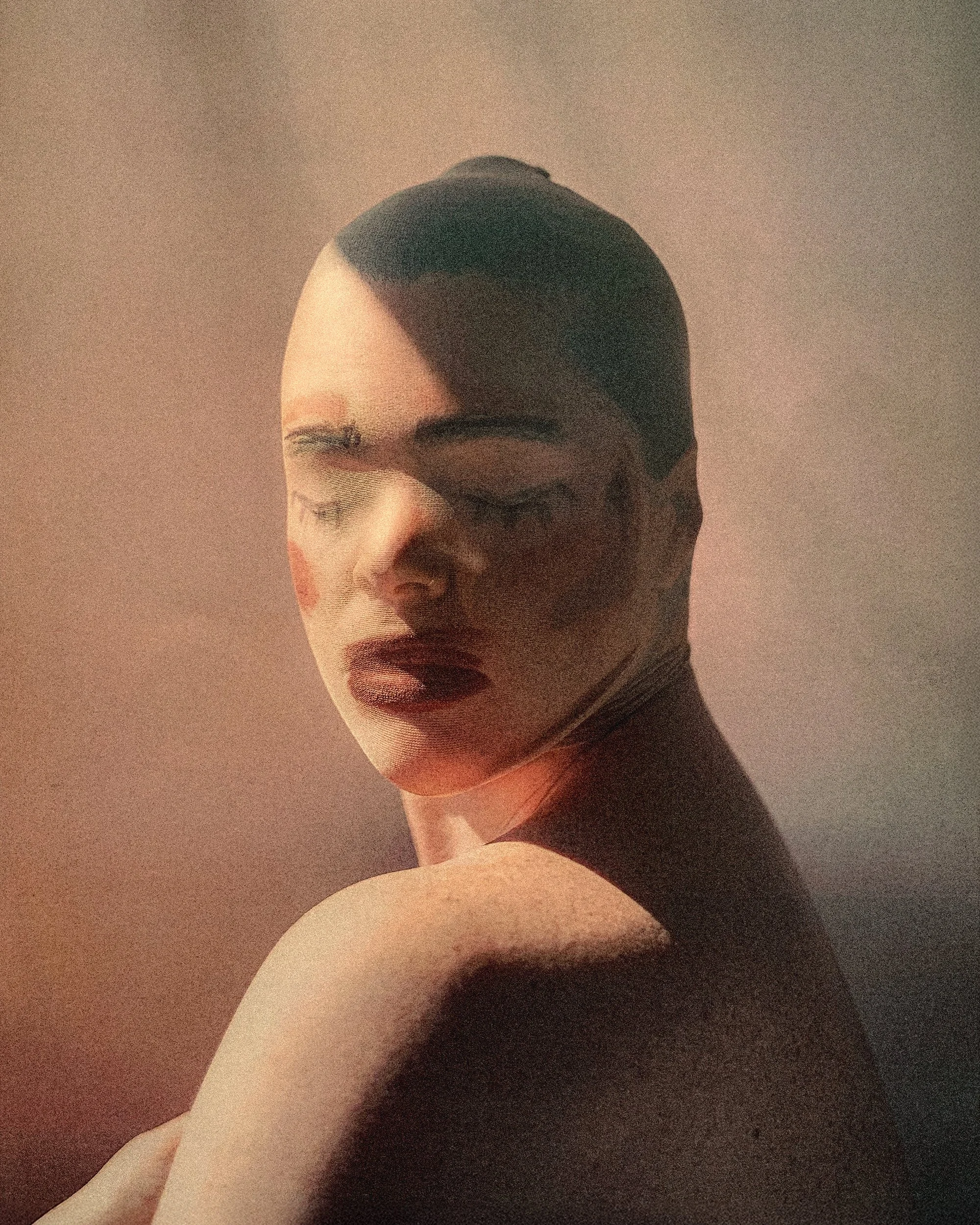 A person with short dark hair, closed eyes, and makeup, including dark lipstick, shown in a close-up portrait with a soft light and background.