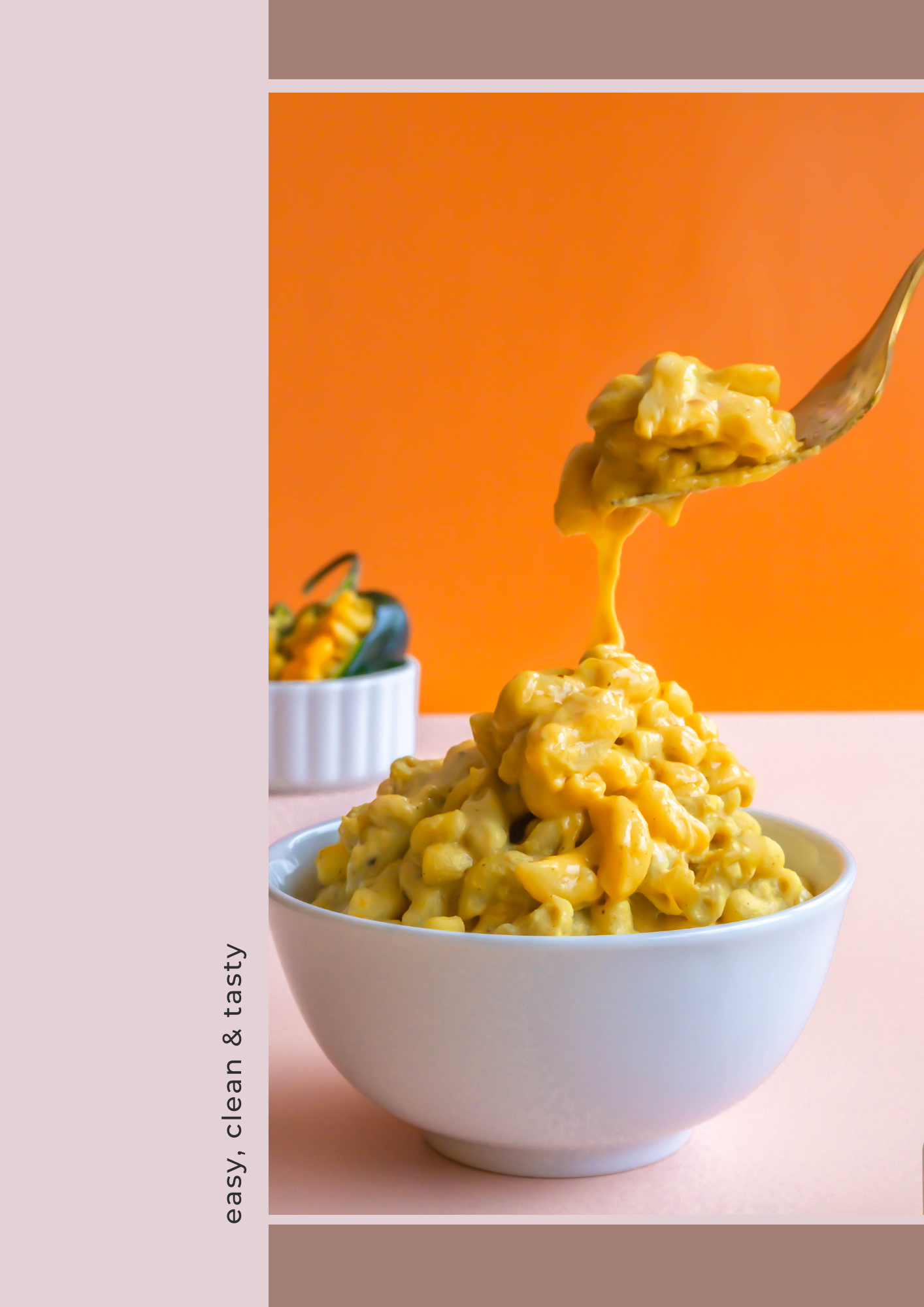 A white bowl filled with cheesy macaroni and cheese on a light pink surface, with a fork lifting some of the pasta. In the background, there is a small white bowl with some herbs and vegetables, set against an orange wall.