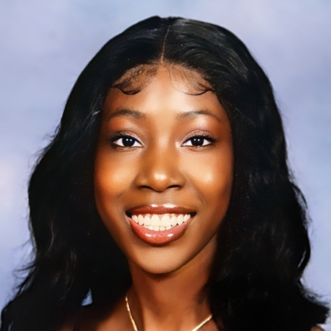 Portrait of a smiling woman with dark hair and gold necklace, light makeup, and a blue background.