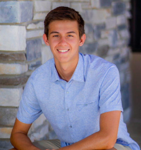 Young man smiling and sitting outdoors against a stone wall.
