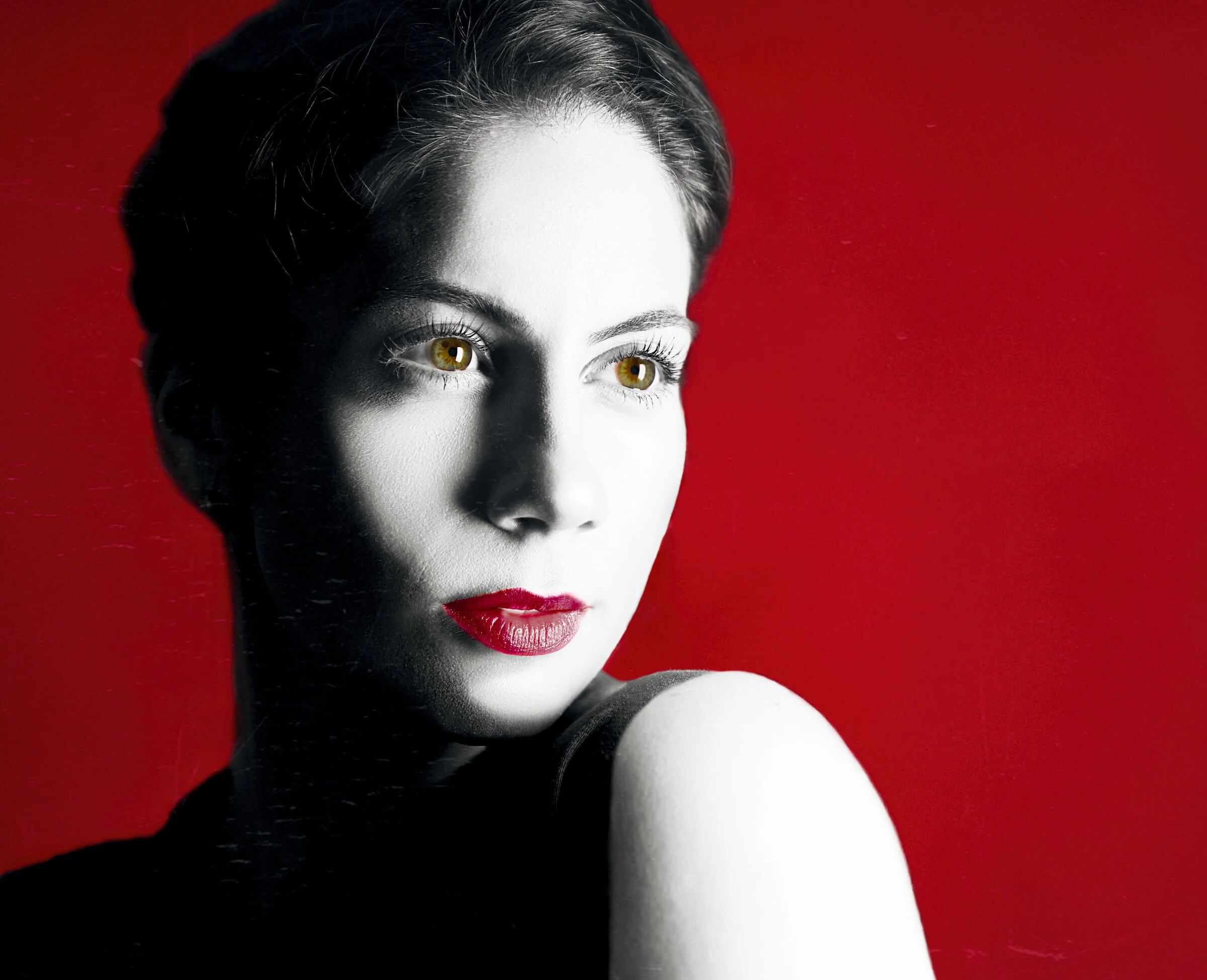 Black and white portrait of a woman with red lipstick and brown eyes, against a red background.