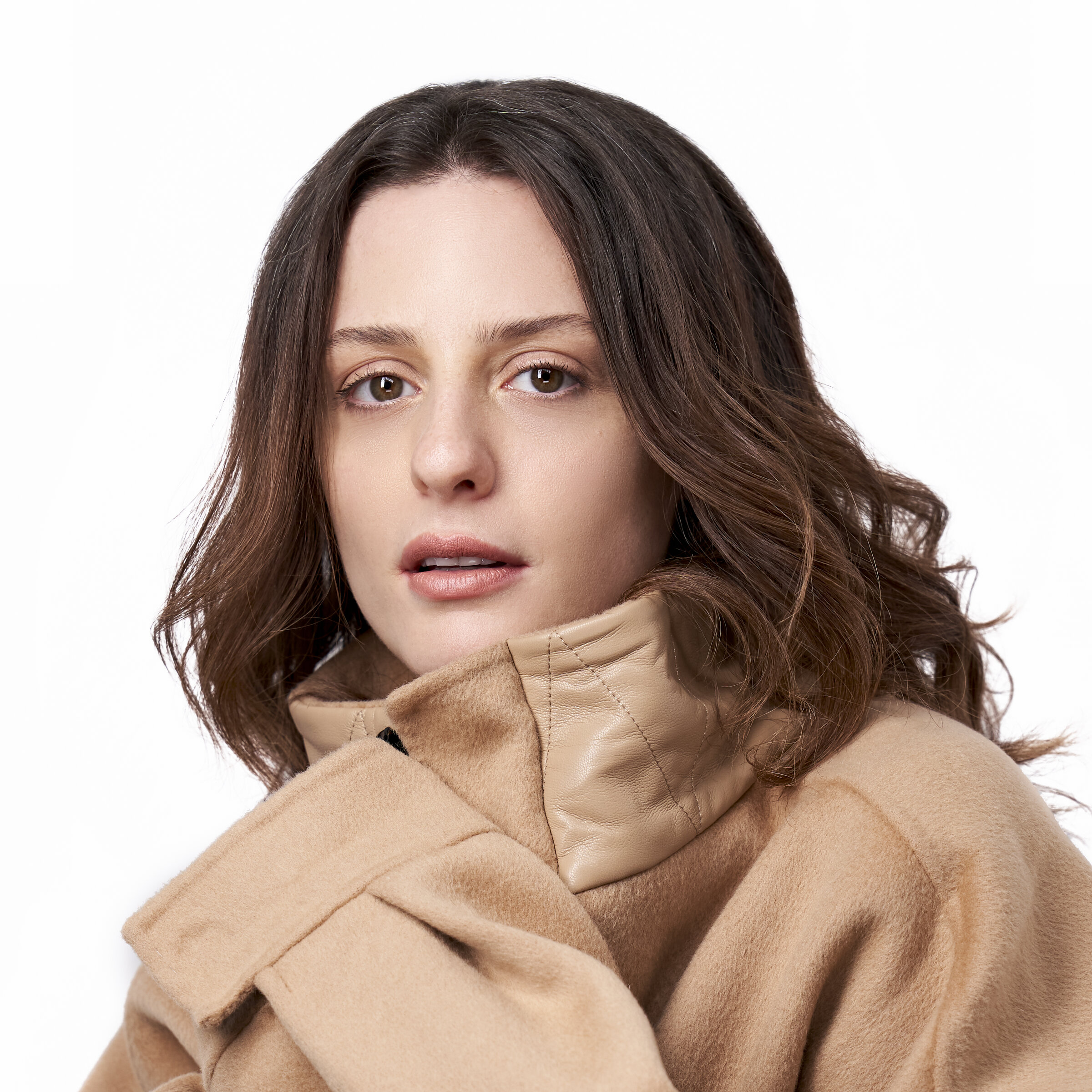 A woman with shoulder-length brown hair wearing a beige coat with a high collar against a plain white background.