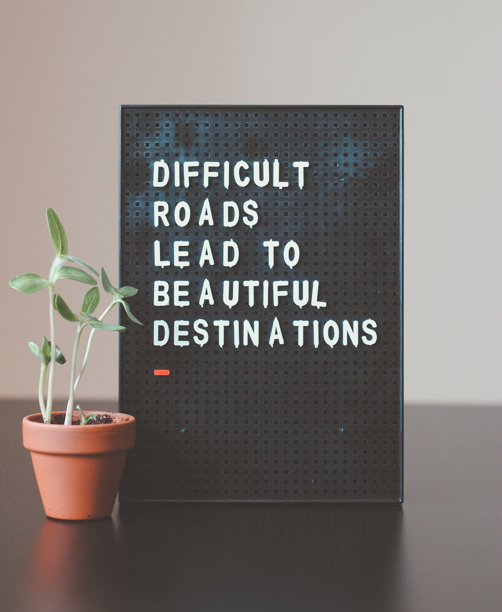 Quote board reading 'Difficult roads lead to beautiful destinations' beside a small potted plant.