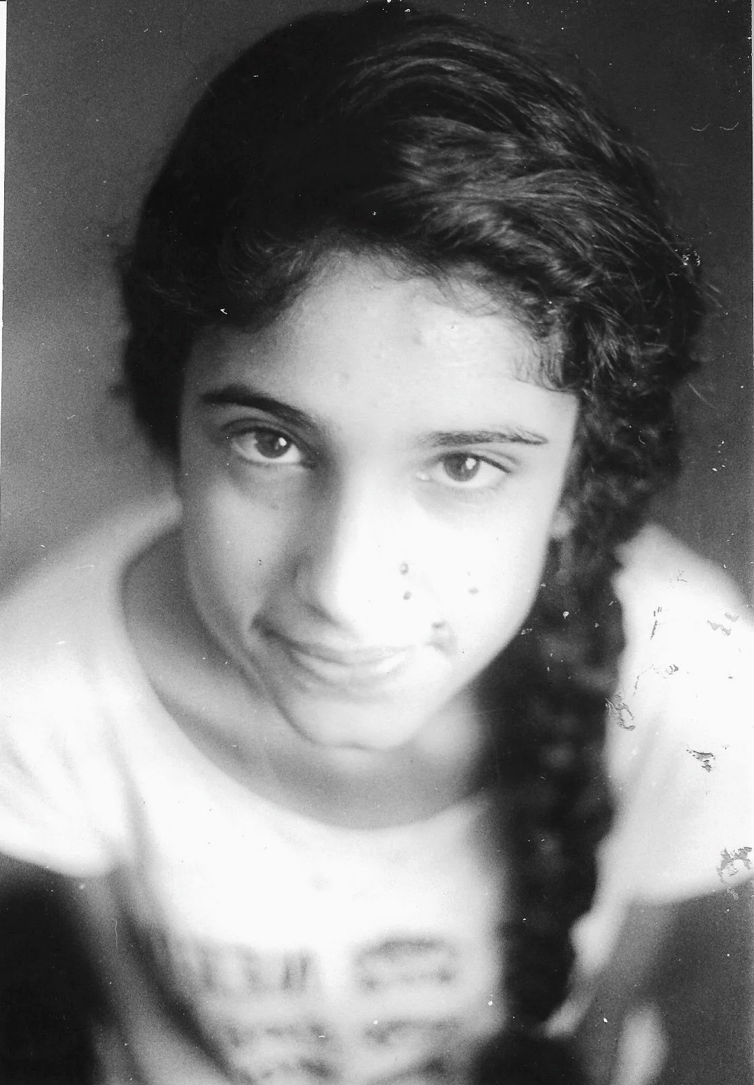 Black-and-white close-up portrait of a young woman with dark, curly hair styled in a braid, looking directly at the camera with a neutral expression.