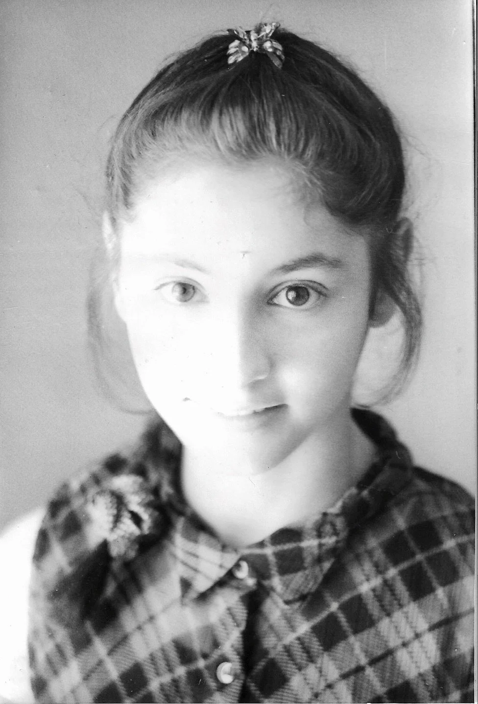 Black and white portrait of a young girl with braided hair, wearing a plaid shirt with a bow-shaped hair accessory.