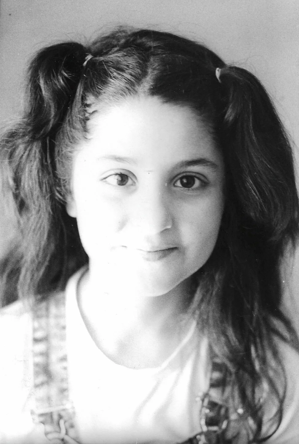 Black and white portrait of a young girl with long, wavy hair styled in pigtails, looking at the camera with a slight smile.
