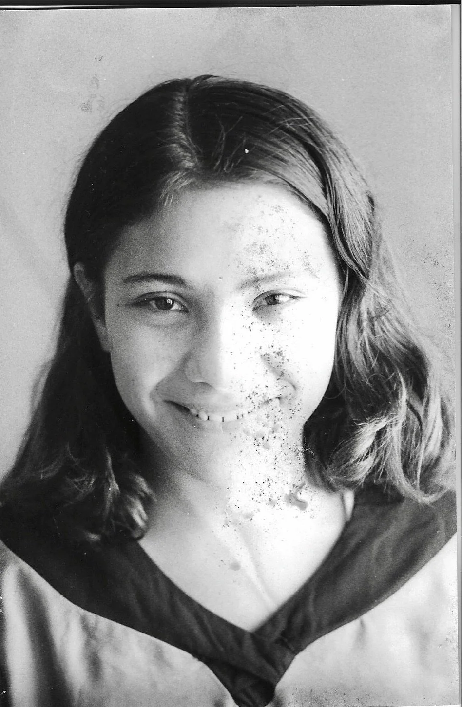 Black and white portrait of a young girl with shoulder-length hair, smiling and looking at the camera.
