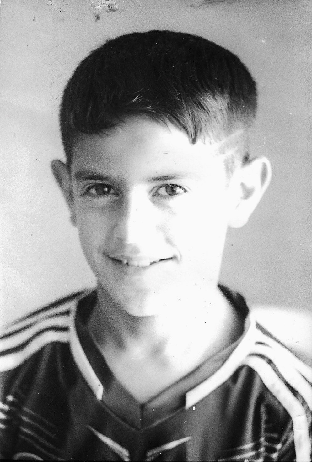 A young boy smiling, wearing a sports jersey with striped design, black and white photo.