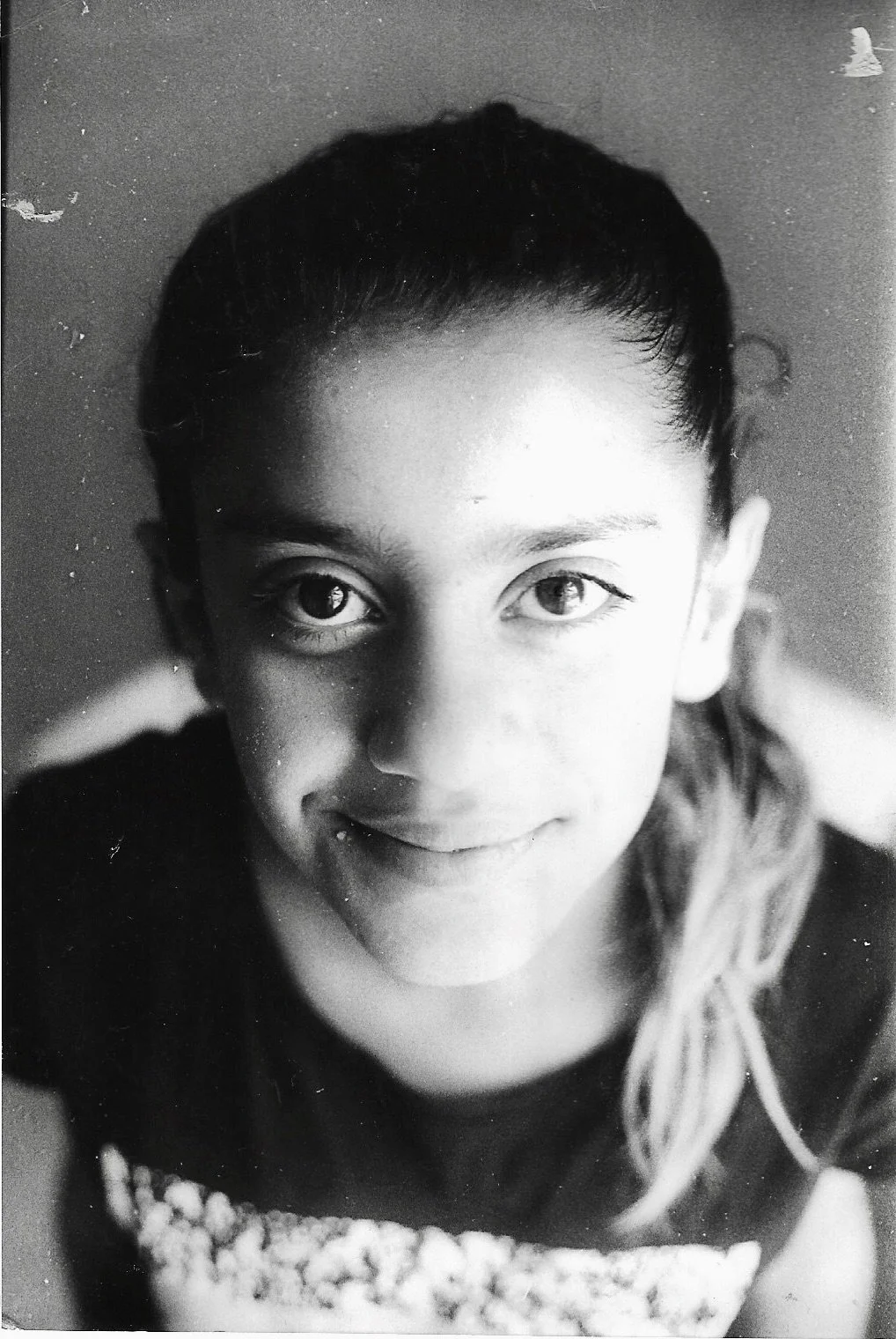 Black and white close-up portrait of a young girl with light-colored eyes and long hair, smiling gently, with her head tilted slightly back.