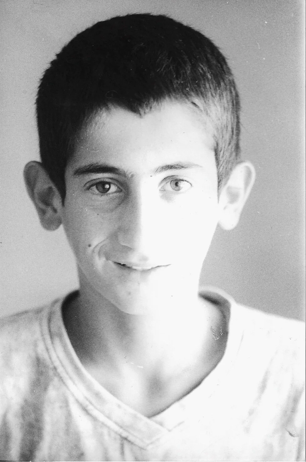 A black and white portrait of a young boy with short dark hair, light-colored eyes, and a slight smile, wearing a light-colored shirt.
