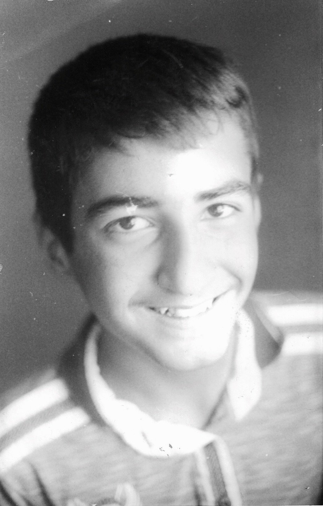 Black and white portrait of a smiling young man with short hair, wearing a striped shirt.