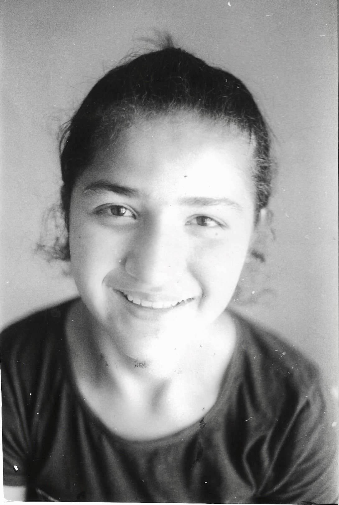 A smiling young woman with dark hair pulled back, wearing a dark top, in black and white.