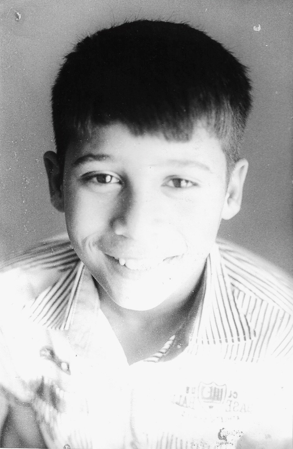 A black and white photo of a young boy with short dark hair, smiling, wearing a striped shirt.