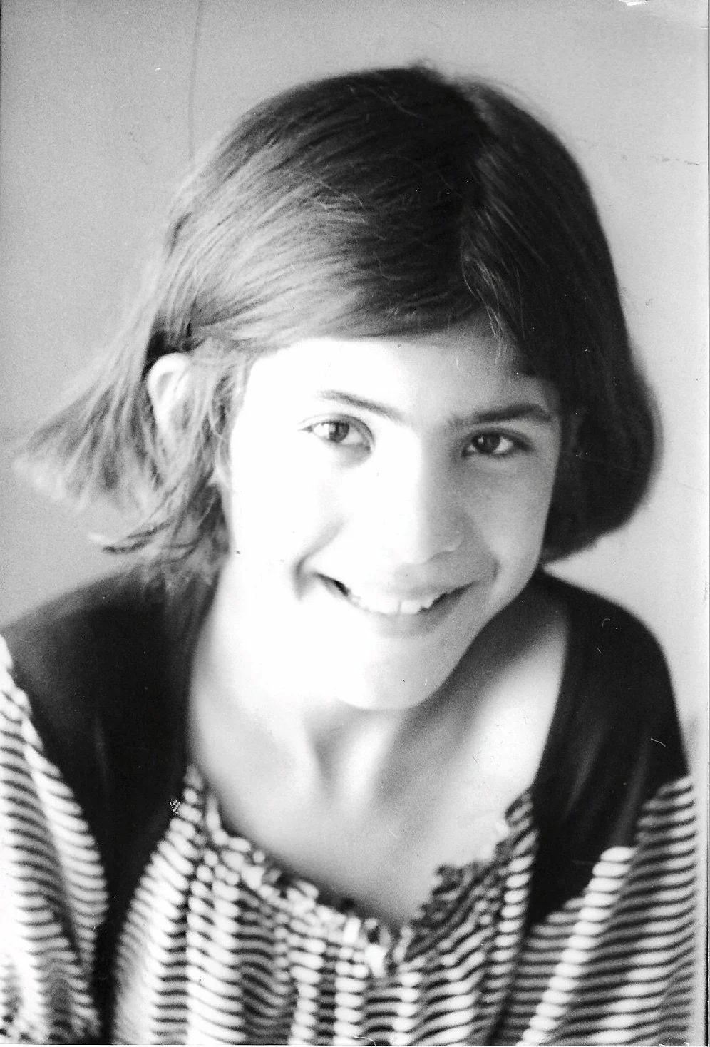 A black and white photograph of a young woman with short, layered hair, smiling at the camera, wearing a striped shirt.