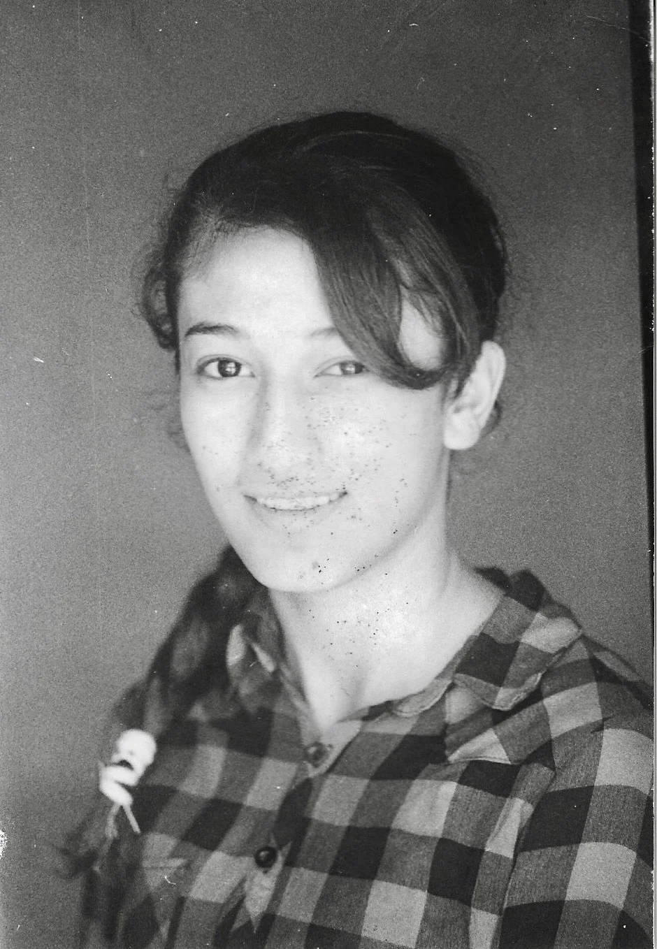 A young man with light skin and freckles, smiling, wearing a checkered shirt, in a black and white photograph.
